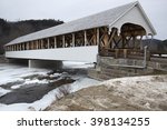 Historic white covered bridge dating to the mid-19th century in Stark, New Hampshire in winter, with ice in the Upper Ammonoosuc River.