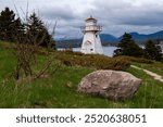 The historic Woody Point lighthouse on Crawley Head overlooking the south arm of Bonne Bay with the town of Norris Point and the Gros Morne Mountain visible in the background.