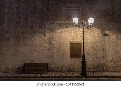 Historical ancient street Lamp and a bench at night with the wall behind them on the old stony pavement on the road with yellow lines