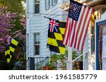 Historical Colonial Era Maryland Flag Calvert Arms Kings Colors featuring checkered yellow and black banner of Lord Baltimore and a Union Jack is hanging side by side with a US flag on a building 