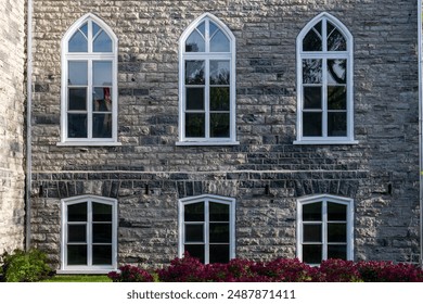 A historical concrete building, Gothic Revival style of architecture with multiple windows. Clean mason style with grey and beige bricks on the frame and has six clerestory cathedral glass windows. - Powered by Shutterstock