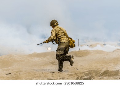 Historical reconstruction. An American infantry soldier from the World War II runs on the beach between smoke and dust.  View from the back.  Hel, Poland 