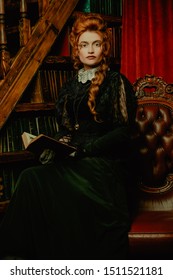 Historical Reconstruction Of The Victorian Era. Portrait Of An Elegant Woman In Vintage  Dress And Hairdo Reading A Book In Her Library. Baroque Era.