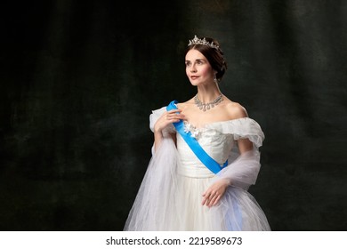 Historical reconstruction. Young queen. Portrait of adorable girl in image of medieval royal person in renaissance style dress isolated on dark background. Comparison of eras, beauty, history, art. - Shutterstock ID 2219589673