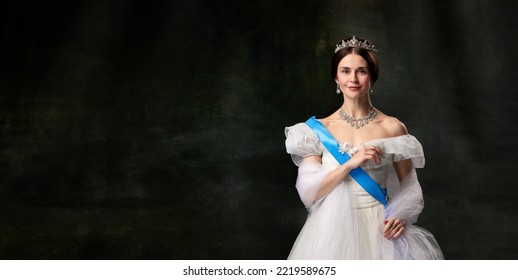 Historical reconstruction. Young queen. Portrait of adorable girl in image of medieval royal person in renaissance style dress isolated on dark background. Comparison of eras, beauty, history, art. - Shutterstock ID 2219589675