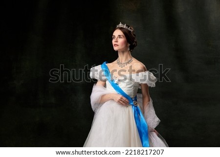 Historical reconstruction. Young queen. Portrait of adorable girl in image of medieval royal person in renaissance style dress isolated on dark background. Comparison of eras, beauty, history, art.