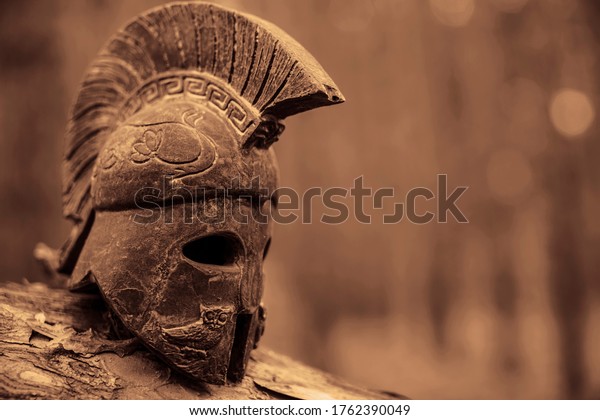 Historical Replica\
Spartan Warrior Helmet on pine forest background. Close up view of\
small miniature roman helmet\
