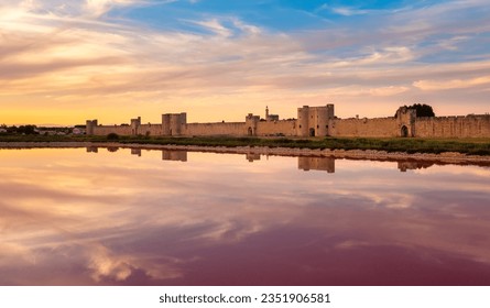 Historical walled town Aigues-Mortes reflecting in a pink salt lake on sunset, Camargue region, southern France