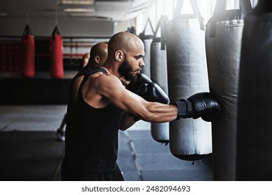 Hit, punching bag and man in gym with boxing gloves for workout, challenge or competition training. Power, muscle and champion boxer in exercise with confidence, fitness and energy in MMA sports club - Powered by Shutterstock