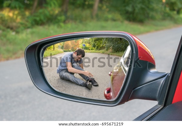 Hit and run concept. View on injured man on road in\
rear mirror of a car.