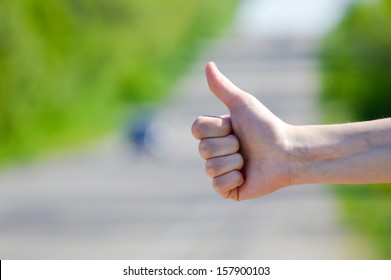 Hitchhiker Sign Thumb Up At Road Background On Summer Day