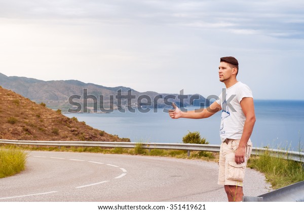  hitchhiker\
young man, hitchhiking on a rural road hitchhiking on the\
background of the road, blue see and sky\
