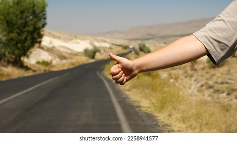 Hitchhiking, close-up of a woman's hand with thumb up against the background of a suburban road. A highway policeman stops a car on the highway. Travelling alone on an easy road. Summer