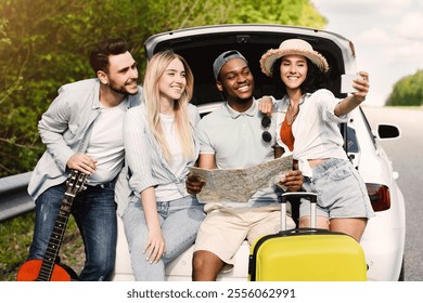 Hitchhiking concept. Group of young friends looking at map during road trip, taking selfie while sitting in car trunk on highway, copy space. Diverse students resting on roadside after long drive - Powered by Shutterstock