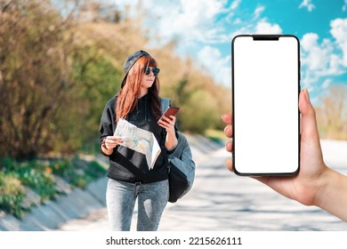 Hitchhiking. Hipster Girl In Cap And Sunglasses Stand Along The Road With A Paper Map And Using A Smartphone. Female Hands Holding A Smartphone With Mock Up. Concept Of Online Map.