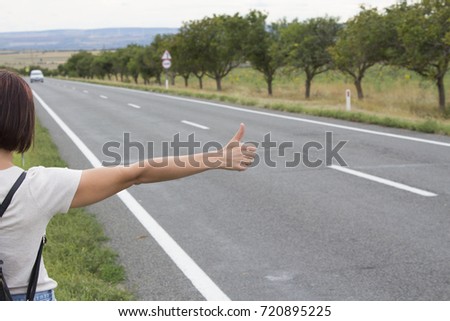 Hitchhiking the road. Female hand gesture,  road trip, travel. Young woman with a backpack hitch-hiking on a road at the fields. concept of people.