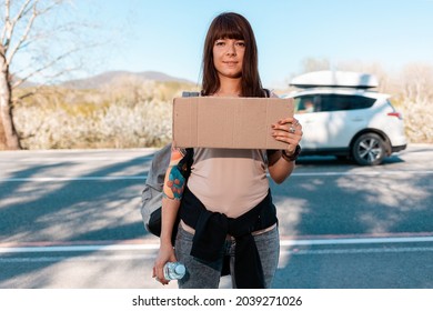 Hitchhiking. Smiling caucasian young woman with tattoed hand holding a cardboard sign with mock up. Copy space. The concept of local traveling.