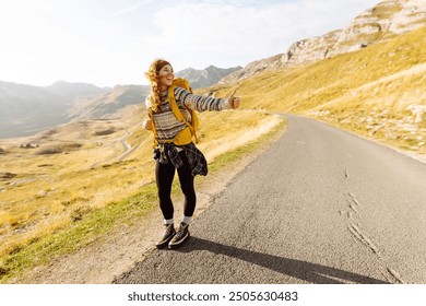 Hitchhiking woman traveler try to stop car on the mountain road. Travel and vacation theme - Powered by Shutterstock