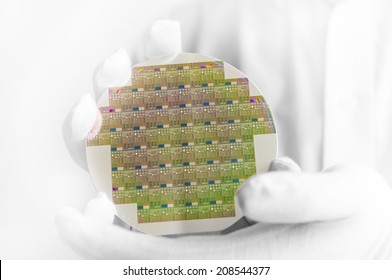 A hi-tech industry engineer in white gloves holding a silicon wafer inside a clean room lab.