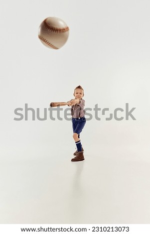 Hitting. Boy, child in classical retro clothes playing baseball over grey studio background. Concept of game, childhood, friendship, activity, leisure time, retro style, fashion.