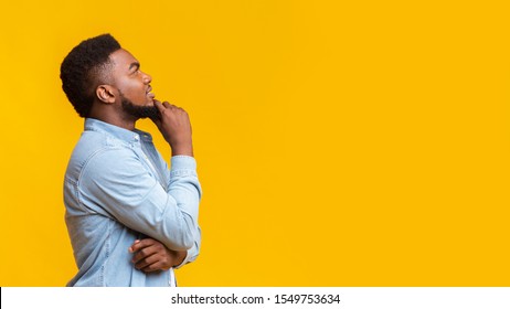 Hm, interesting offer. Profile portrait of black millennial guy thinking about something and looking upwards at copy space, panorama