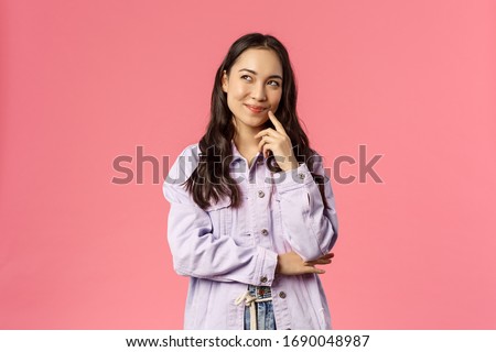 Hmm interesting. Portrait of smiling creative girl in denim jacket, thinking, have intriguing idea, smirk and look upper left corner, daydreaming, planning something for party, pink background