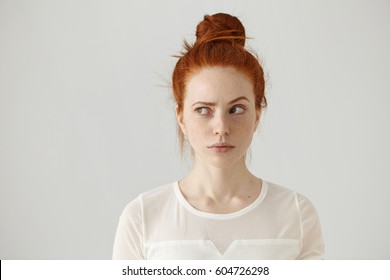 Hmm. Let me think. Studio shot of cute redhead girl with hair knot and freckles looking sideways with thoughtful and sly expression, raising one brow as if having good idea, planning something