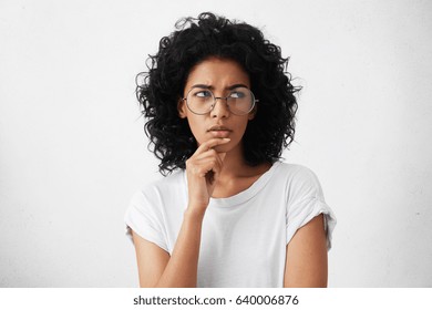 Hmm. Suspicious Thoughtful Young Mixed Race Female With Black Curly Hair Looking Up, Keeping Hand On Her Face As If Trying Hard To Remember Something Important. Human Face Expressions And Emotions