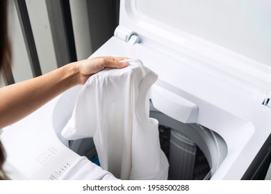 Hnads of young woman putting white color clothes into washing machine at condominium. Laundry concept. Top view