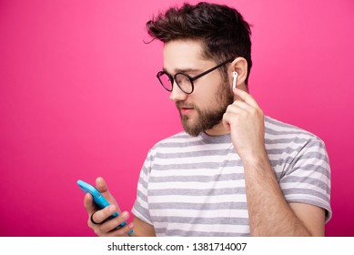 Hnadsome aman wearing glasses, using airpods, over isolated pink packground 