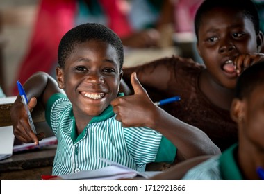 Ho, Asogli / Ghana - September 15, 2018: A Smiling Bright Young Female Student In Uniform With Pen In Hand Gives A Big Smile And Thumbs Up Sign For A Classroom Picture.