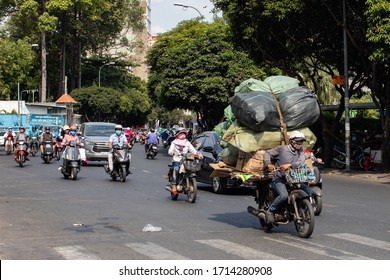 Ho Chi Minh city, Saigon, Vietnam; February 2020: Overloaded scooter with stuff driving on the dense traffic in the streets of the city, drivers wearing helmets and face masks
