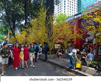 Ho Chi Minh city, Vietnam - Jan 22, 2016: : Atmosphere of springtime with colorful scene on Saigon street, Vietnamese woman in ao dai, posing beside flower to take photo on Tet holiday
