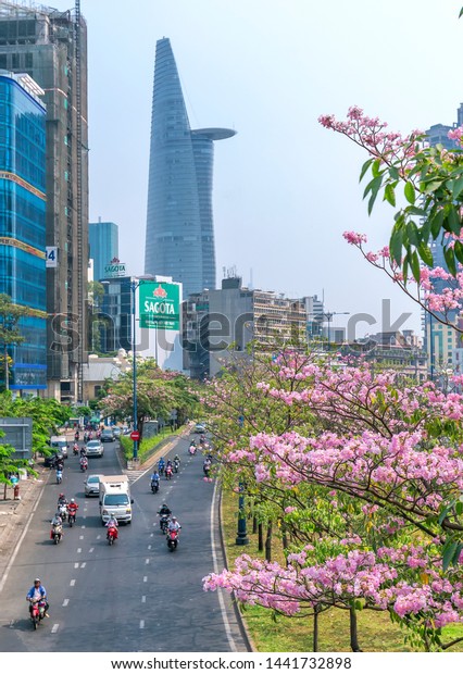 Ho Chi Minh city, Vietnam, March 16th, 2019:\
Traffic in Saigon from high view, street with motorbikes, car move\
under pink tabebuia rosea flower tree of developed city in Ho Chi\
Minh City, Vietnam