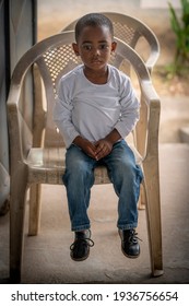 Ho, Ghana - September 16, 2018: Too Small To Touch The Floor, A Little Boy Sits In A Plastic Chair In Ghana, West Africa.