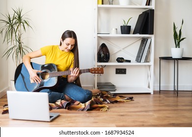 Hobbies and leisure activities during quarantine. Online training, online classes. A young woman watches a video lesson on playing the guitar, she sits on a cozy plaid with a guitar
