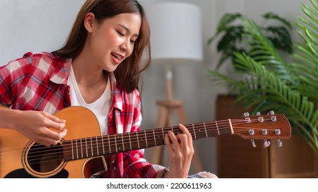 Hobby concept, Young asian woman learning and practice playing chords with acoustic guitar on couch.
