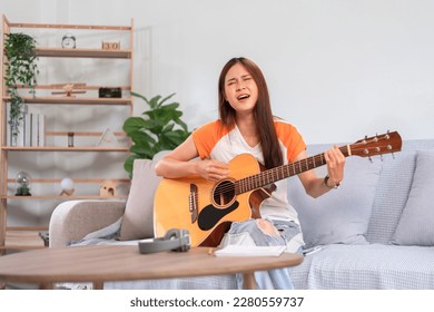 Hobby concept, Young asian woman sitting on couch to singing and playing music with acoustic guitar.
