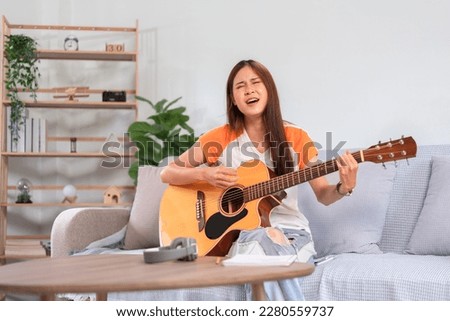Hobby concept, Young asian woman sitting on couch to singing and playing music with acoustic guitar.