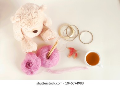 Hobby Craft Kit Of Wired-up Wooden Knitting Needles, Two Pink Color Mohair Yarn Balls. Creamy Color Teddy Bear, Cup Of Tea, Colorful Fruit Jelly, Four Bracelets. On Even Vanilla Color Background.