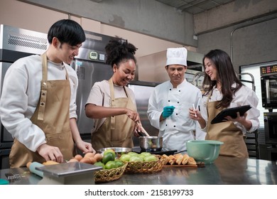 Hobby cuisine course, senior male chef in cook uniform teaches young cooking class students to prepare, mix and stir ingredients for pastry foods, fruit pies in restaurant stainless steel kitchen. - Powered by Shutterstock