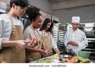 Hobby cuisine course, senior male chef in cook uniform teaches young cooking class students to peel and chop apples, ingredients for pastry foods, fruit pies in restaurant stainless steel kitchen. - Powered by Shutterstock