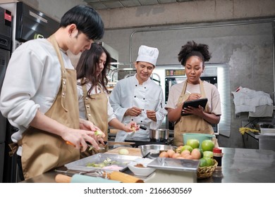 Hobby cuisine course, senior male chef in cook uniform teaches young cooking class students to peel and chop apples, ingredients for pastry foods, fruit pies in restaurant stainless steel kitchen. - Powered by Shutterstock