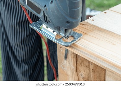 A hobbyist DIY carpenter cutting a plank of wood with a jigsaw - a type of power tool with a reciprocating blade - Powered by Shutterstock