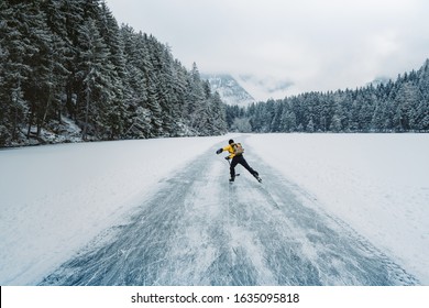 A hockey player shooting the puck as he speeds down the ice. Ice skating in nature. Scenic panoramic view of the silhouette of a young hockey player skating on a frozen lake. Travel and sports