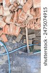 A hoe wooden handle placed among scattered bricks and a blue hose at the construction site