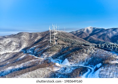 Hoengseong-gun, Gangwon-do, South Korea - March 03, 2021: Aerial View Of Snow Covered Curve Road And Turbines On Wind Farm Of Taegisan Mountain Against Blue Sky
