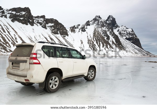 HOFN, ICELAND - FEBRUARY 24,\
2016: Winter off road driving in Iceland, white jeep Toyota Land\
Cruiser on ice near the Vestrahorn mountain at Stokksnes\
Peninsula.
