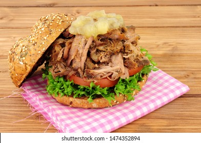 Hog roast meat sandwich with apple sauce and salad in a seed covered bread roll on a wooden background