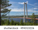 Hoga Kusten or High Coast Bridge from the north bank of the river Angermanalven in eastern Sweden. Trees in foreground and partly cloudy blue skies in the background.